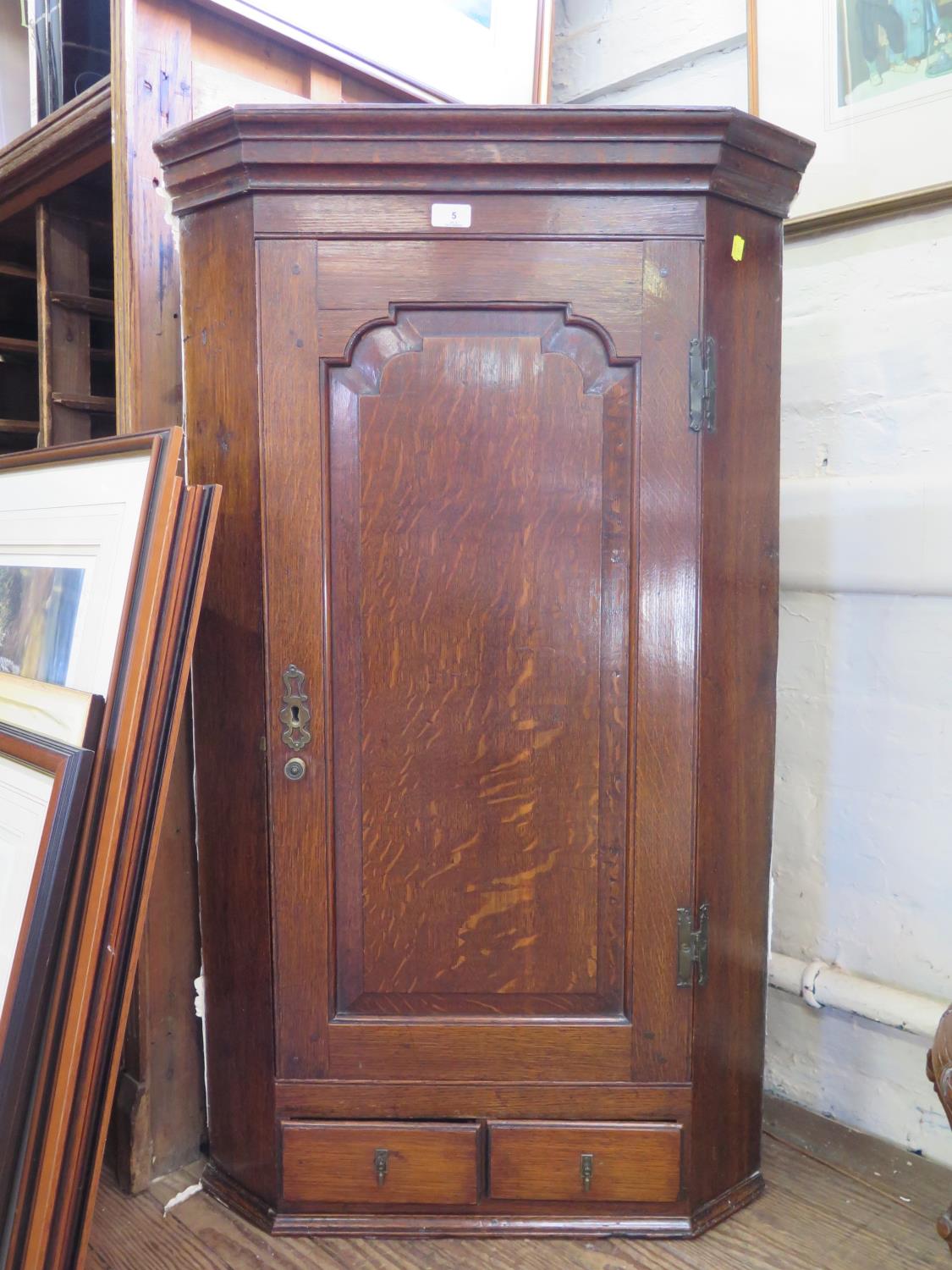 A George III oak hanging corner cabinet, the panelled cupboard door enclosing shaped shelves over