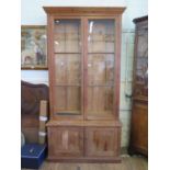 A pine bookcase cabinet, the moulded cornice over a pair of glazed doors enclosing two banks of