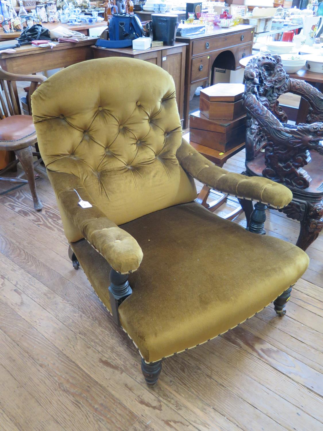 A Victorian ebonised button back deep armchair, with curved arms, turned supports and legs on pot