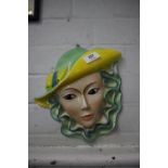 A Shorter and Son Pottery wall mask of a young lady wearing bright green and yellow hat