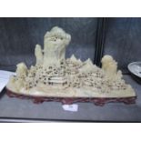 A Chinese soapstone sculpture of houses under trees and rocky mountains, on a red hardstone base, 52