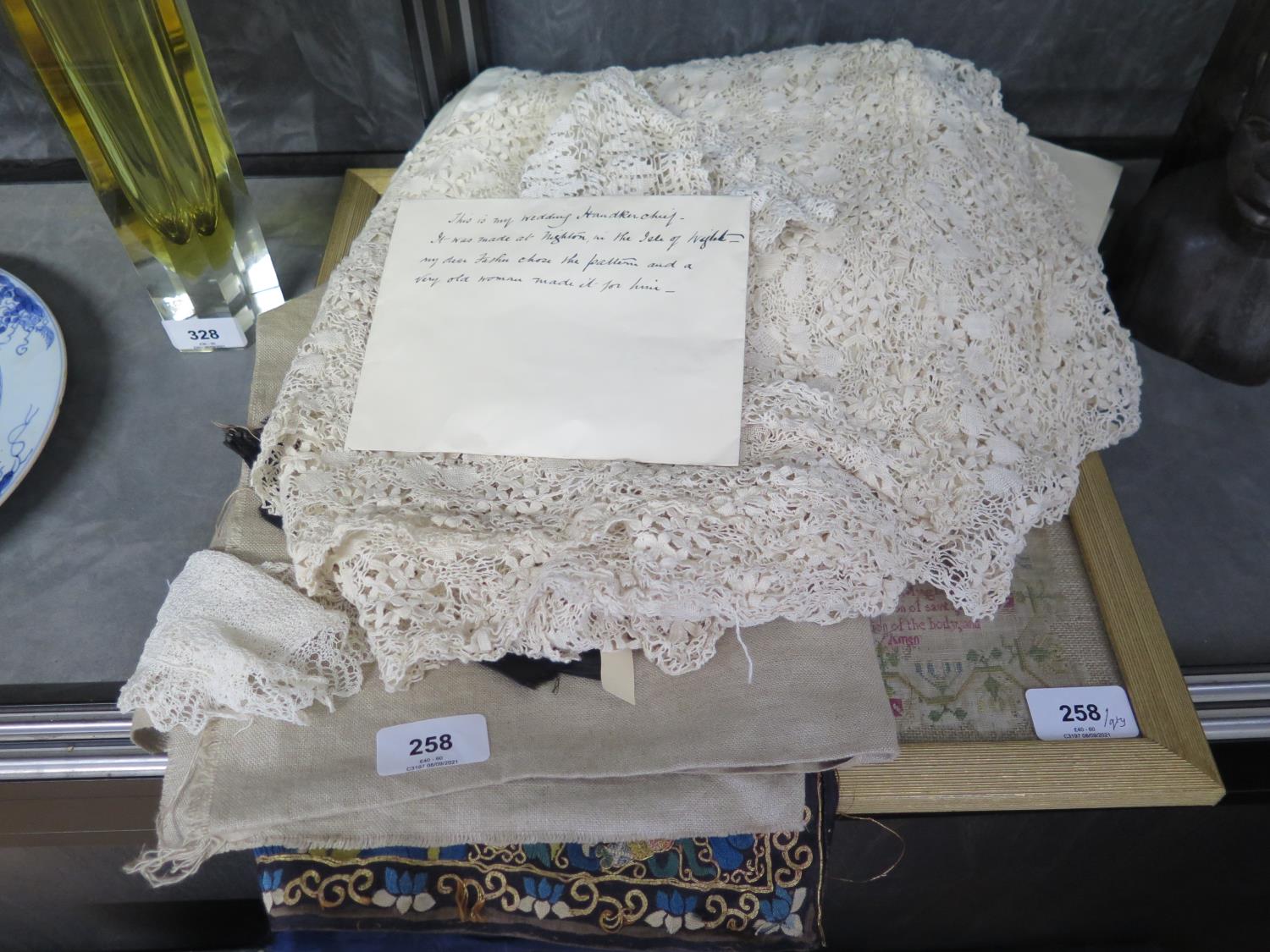 A 19th century lace table cloth, a child's lace bonnet, other textiles and a framed sampler