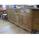 A pine dresser base, with four short drawers over two pairs of panelled doors on a shaped plinth