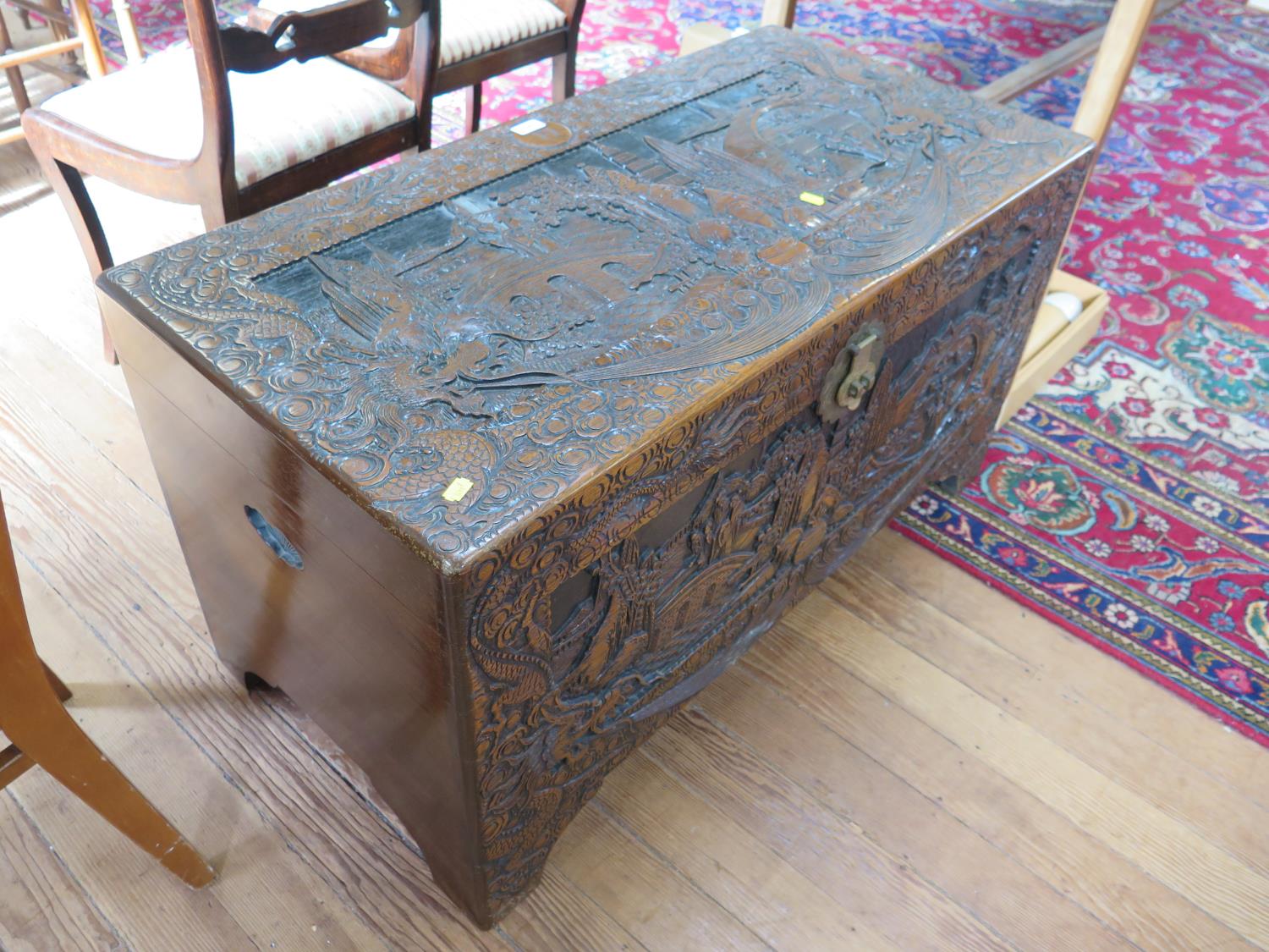 A Chinese carved camphorwood chest, the hinged lid depicting figures in gardens, within a dragon