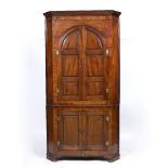 A GEORGE III MAHOGANY FLOOR STANDING CORNER CUPBOARD the top section with arching panel doors