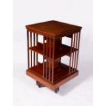 AN EDWARDIAN WALNUT ROTATING BOOKCASE with cast iron brackets to the stand and on ceramic casters,