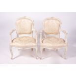 A PAIR OF FRENCH CREAM PAINTED OPEN ARMCHAIRS with upholstered backs and seats, cabriole legs,