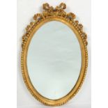 A 20TH CENTURY GILDED OVAL WALL MIRROR decorated with a ribbon swag, 55cm wide x 88cm high