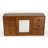 AN OAK ARTS AND CRAFTS TABLE TOP CABINET with central mirrored door flanked by six small drawers,