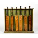 A GREEN PAINTED WOODEN CRICKET BAT STAND complete with six vintage cricket bats, the green painted