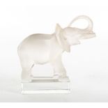 A LALIQUE MOULDED GLASS ORNAMENT in the form of an elephant with raised trunk, standing in a