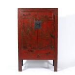 AN ORIENTAL RED LACQUERED TWO DOOR CUPBOARD the doors painted with buildings amongst Oriental