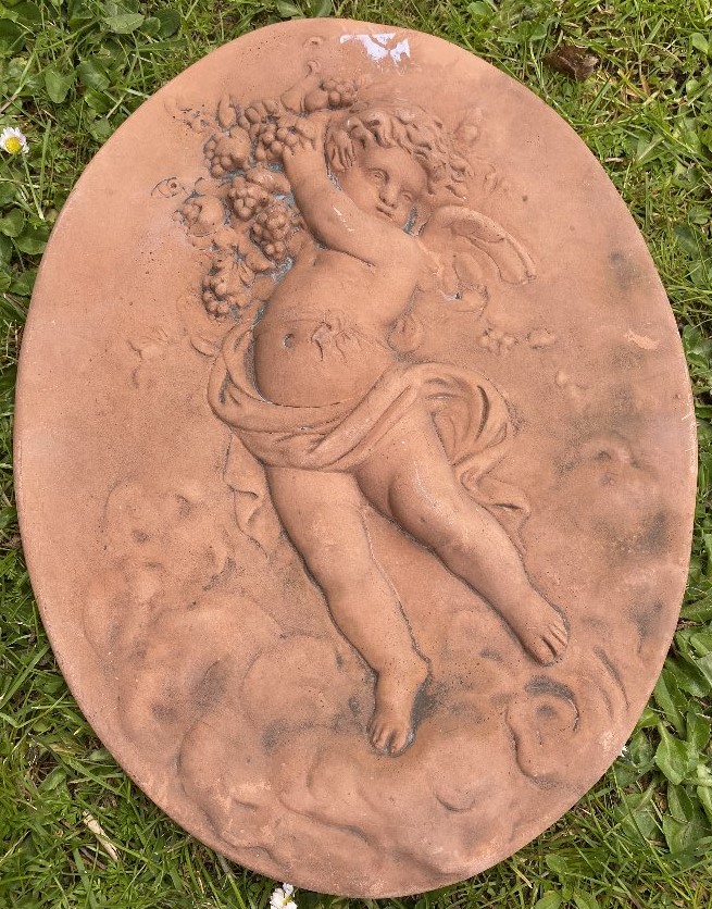 AN OVAL TERRACOTTA TYPE MOULDED WALL PLAQUE depicting a cherub with grapes, 37cm x 28cm Condition: