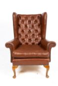 AN EARLY TO MID 20TH CENTURY BROWN LEATHER BUTTON UPHOLSTERED WING BACK ARMCHAIR with cabriole legs,