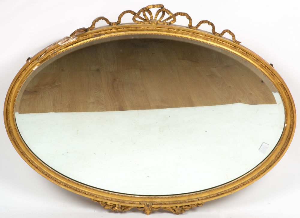 AN OVAL GILT WALL MIRROR with ribbon cresting, 89cm wide x 96cm high overall together with a cream