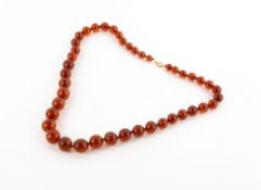 AN AMBER BEAD NECKLACE with a yellow metal clasp stamped 750, the largest bead 15mm diameter At