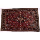 Persian red ground rug with central blue medallion and foliate border, 204cm x 125cm