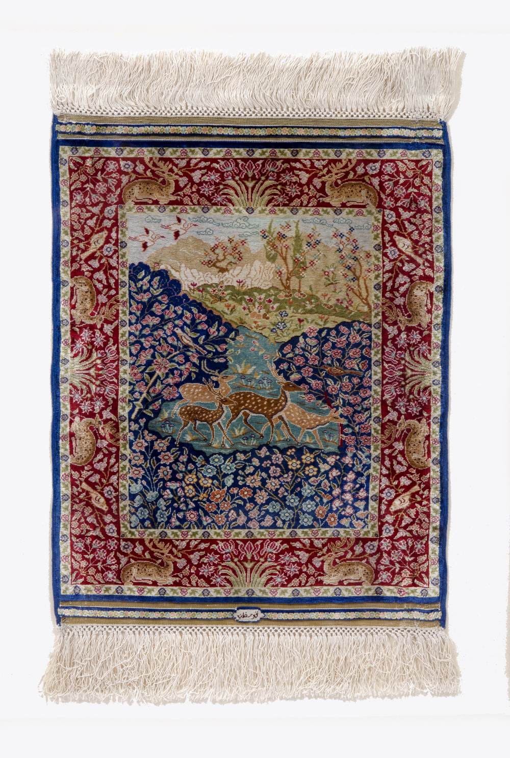 A PERSIAN MINIATURE SILK RUG woven with deer in a landscape pattern in colours within a red border - Image 2 of 2