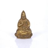 A TIBETAN GILT BRONZE BUDDHA, with raised hand sat upon a lotus base in a traditional gown, 7cm long