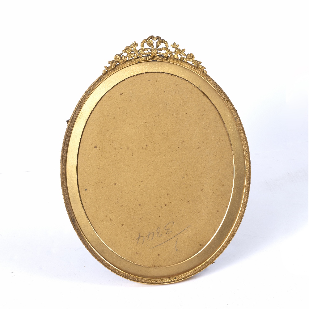 A GILT METAL OVAL PORTRAIT FRAME with ribbon swag cresting and easel support, green velvet back by