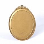 A GILT METAL OVAL PORTRAIT FRAME with ribbon swag cresting and easel support, green velvet back by