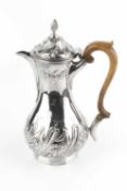 A George III silver baluster hot water pot, embossed and engraved with spiral lobes and foliage,