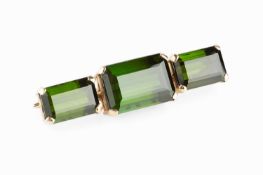 A green tourmaline three stone brooch, the rectangular step-cut tourmalines in four claw settings,