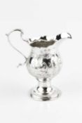 A George III silver cream jug, with baluster body embossed and engraved with a continuous village
