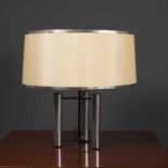 A contemporary chrome plated table lamp with three cylindrical legs with supports going to a central