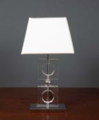 A contemporary glass and white metal plated table lamp with two hollow square sections and on a
