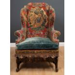 A James II walnut wing armchair with an eared back and outstretched scrolling arms, covered in