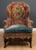 A James II walnut wing armchair with an eared back and outstretched scrolling arms, covered in