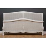 A modern white painted French style king size bed with floral carved arching cresting rail and caned