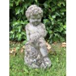 A small reconstituted stone fountain head in the form of a boy, seated on a rocky outcrop with