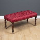 A mahogany stool with turned tapering legs and overstuffed red button upholstered seat, 98cm wide