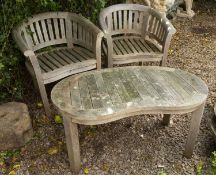 A pair of teak horseshoe shaped garden chairs together with a kidney shaped low table to match,