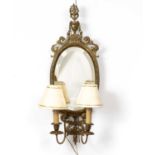 An Adam style brass girandole wall mirror with oval bevelled mirror plate beneath an urn crest and