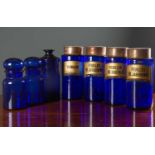 A set of four blue glass cylindrical pharmacy jars with gilt labels and possibly later tin covers,