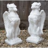 A pair of white painted cast reconstituted stone gate finials in the form of seated griffins, 55cm