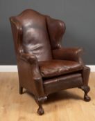 A George III style leather upholstered wing back armchair with arching back, squab cushion and