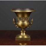 A gilt brass urn of campana form, with foliate handles, with a cut out to the base when used at