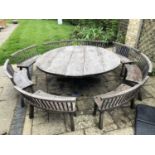 A large circular oak garden table and eight matching curved benches to seat sixteen, the table on