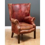A George II style leather upholstered wing back armchair with curving back, scrolling arms and