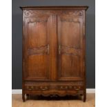 An antique French armoire, the twin panelled doors with shaped tops and carved ornament above two