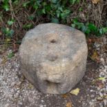 An ancient gritstone quern with mask decoration, the face with open mouth as an aperture for