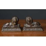 A pair of small cast brass or bronze recumbent lion ornaments each on a square base, 10cm