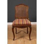 A French walnut side chair with carved frame, caned back and seat and cabriole legs, with striped