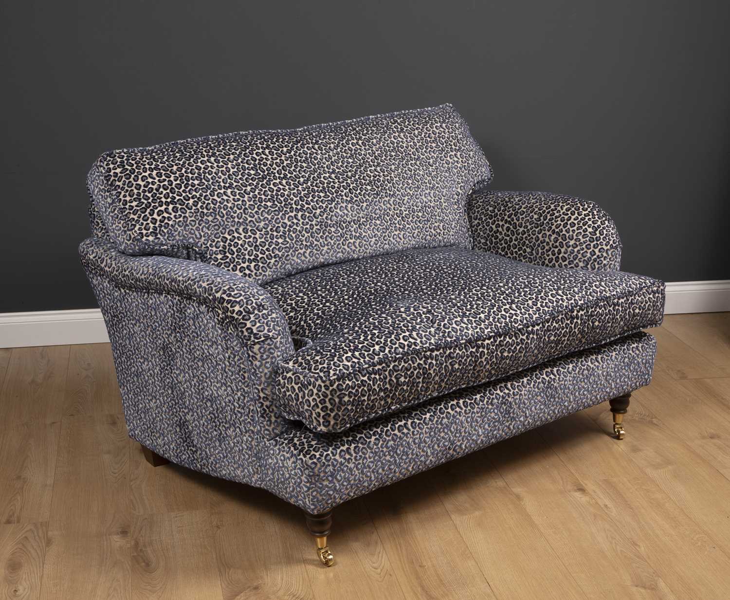 A small modern deep two seater sofa with turned front legs and brass casters, upholstered in lilac