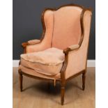 A French carved beechwood framed wing back armchair with scrolling arms and turned fluted tapering