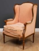 A French carved beechwood framed wing back armchair with scrolling arms and turned fluted tapering